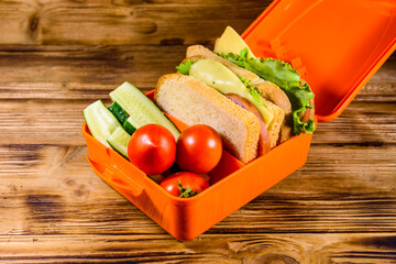Lunch box with sandwiches, cucumbers and tomatoes on wooden table
