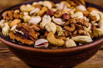 Various nuts (almond, cashew, hazelnut, pistachio, walnut) in ceramic plate on a wooden table. Vegetarian meal. Healthy eating concept
