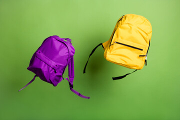 Two school back packs modern style sacks thrown up air on green color background season low prices sale concept children stuff equipment