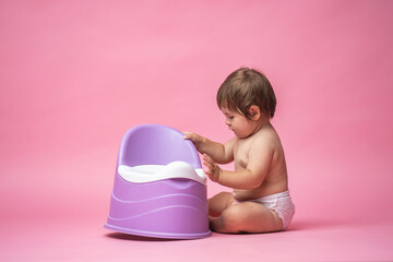 cute baby in a diaper is sitting next to a pot. Toilet and potty training.
