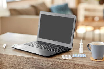 healthcare, technology and medicine concept - laptop computer, drugs and cup on table at home