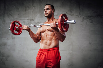 Fototapeta na wymiar Handsome sportive guy with huge biceps and naked torso lifting barbell in custom grung background.
