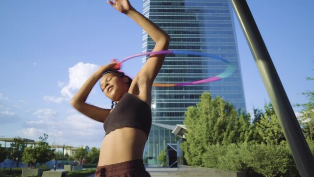 Sporty woman exercising with hula hoop in city