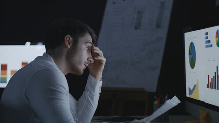 Angry business man throwing document paper on computer table in dark office