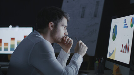 Thoughtful business analyst researching graphs and charts in night office