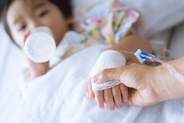 Hands of mother and sick Asian little boy holding together on sickbed in hospital to give encouragement. Healthcare medical.