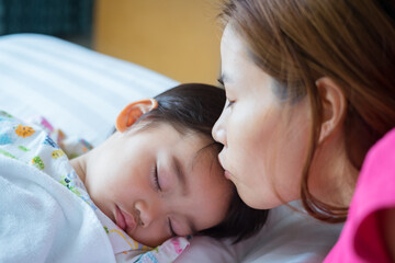 Asian cute little boy patient is sleeping on the sickbed and the face with tears, his mother kissed him on the forehead in the patient room in hospital. Healthcare medical and people concept.