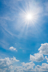 Vertical image of sun on blue sky with sunbeams and clouds in the day