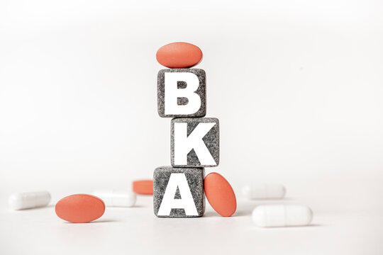 a group of white and red pills and cubes with the word BKA Below the knee amputation. on them, white background. Concept carehealth, treatment, therapy.