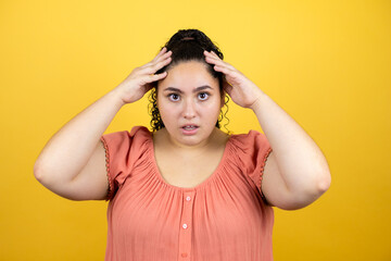 Young beautiful woman with curly hair over isolated yellow background surprised and scared with...