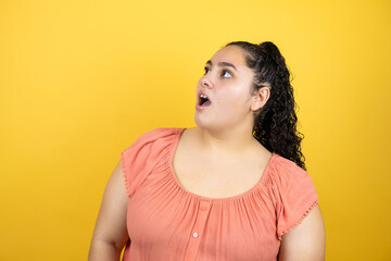 Obraz premium Young beautiful woman with curly hair over isolated yellow background afraid and shocked with surprise expression, fear and excited face.
