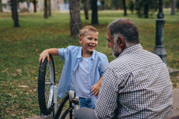 Fototapeta na wymiar grandfather with his grandson at the city park fixing bicycle