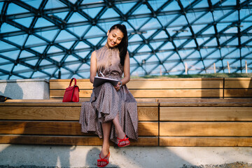 Cheerful female freelancer creating graphic content during remote work in conservatory enjoying own...