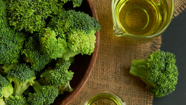 Fresh Broccoli in wooden bowl and seed oil in rustic style. Close up on a black background. copy space for text. Top view, flat lay.