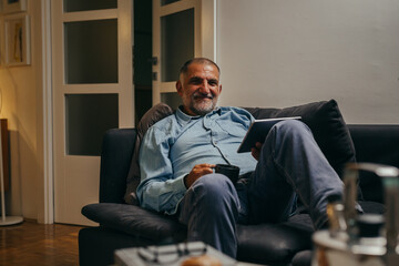 middle aged man sitting sofa using tablet computer at home