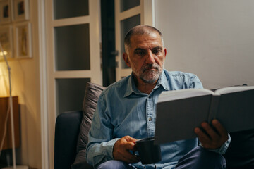 Fototapeta premium middle aged man sitting sofa reading book at home