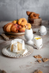soft boiled eggs, fresh cheese and croissants on marble background, fresh peaches, cup of tea, selective focus, traditional breakfast concept