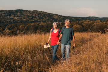 Naklejka na ściany i meble Active senior couple hiking in nature with backpacks, enjoying their adventure at sunset. 