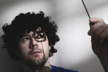 Portrait of an adult man in a black wig with a Halloween pumpkin shadow on his face. Creates creepy...
