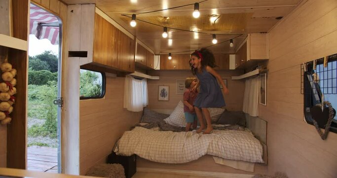 sister and brother having fun and playing together in the trailer house. Siblings jumping on bed