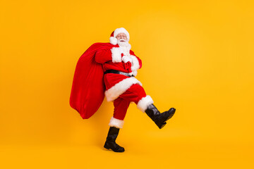 Fototapeta na wymiar Full length body size profile side view of his he nice funny cheerful white-haired Santa St Nicholas going carrying big large sack sale shop isolated bright vivid shine vibrant yellow color background