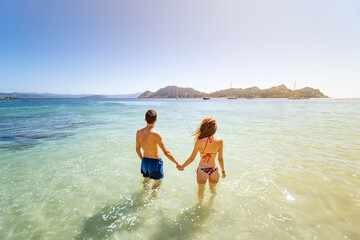 Pareja multi&eacute;tnica en playa paradis&iacute;aca d&aacute;ndose la mano y mirando al horizonte con un precioso color de sol
