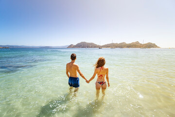 Pareja multiétnica en playa paradisíaca dándose la mano y mirando al horizonte con un precioso color de sol