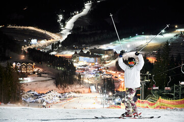 Full length of male skier in winter ski jacket and helmet raising ski poles and looking at camera....