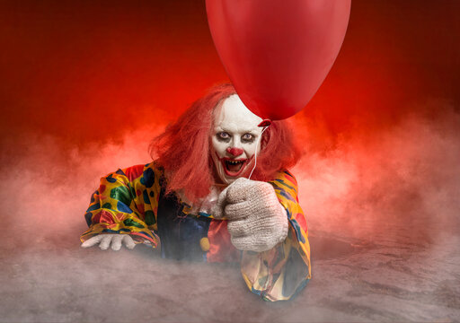 scary clown with a balloon is rising from the sewer