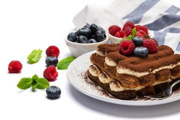 portion of Classic tiramisu dessert with raspberries and blueberries on ceramic plate isolated on white