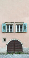 Altes Holztor darüber schöne alte Fenster umrahmt von grünen Fensterläden, rosa Hausfassade, Straße - Pflasterstein,  