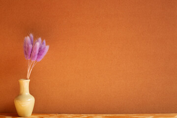 Vase of purple hares tail grass (Lagurus ovatus) dry flowers on wooden table with brown background