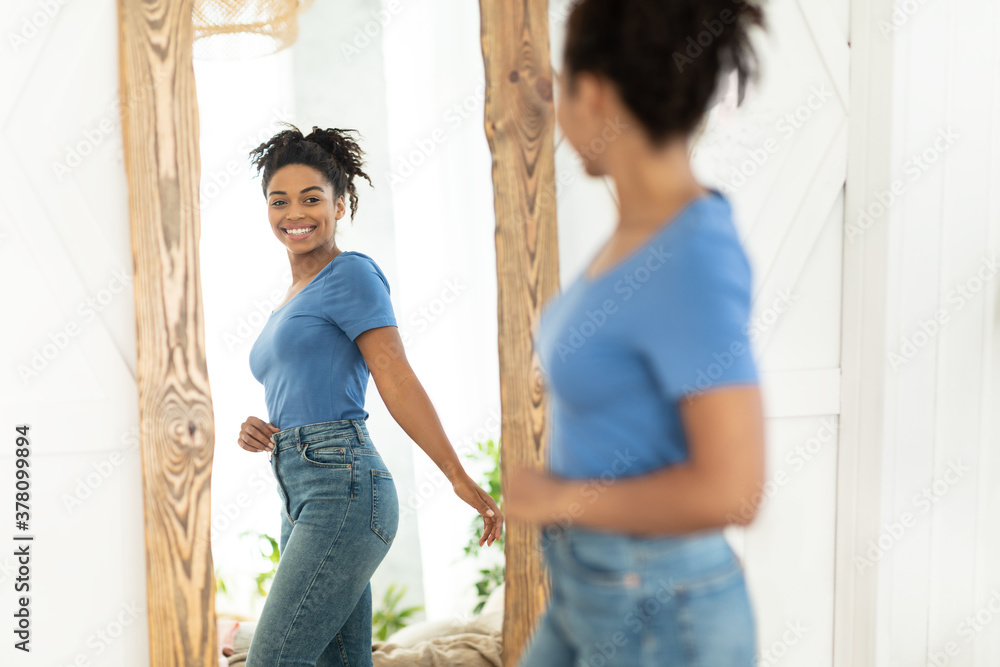 Wall mural joyful african american girl after slimming looking in mirror indoor