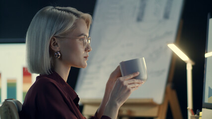 Concentrated business woman drinking coffee front computer in night office