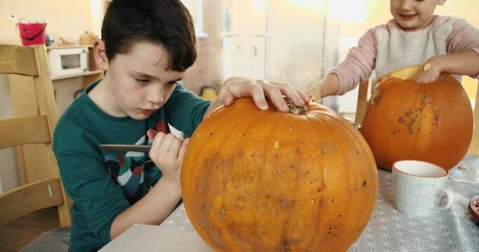 Young boy and girl siblings carving a pumpkin to make a Jack O' Lantern for Halloween
