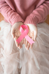 International symbol of Breast Cancer Awareness Month in October. Closeup of female hand holding satin pink ribbon awareness on her knee. Women's health care and medical concept. Copy space. Vertical.