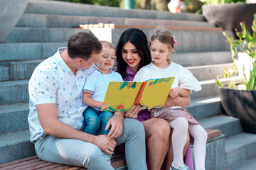Happy young family with two kids sitting in the park reading a book