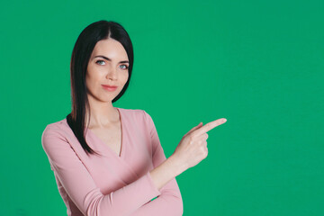 a beautiful girl points her finger. model on a green background. copy space. advertising banner