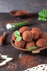 Dark chocolate truffles with raw cocoa powder, mint and fir tree branches, dark brown stone background. Christmas composition.