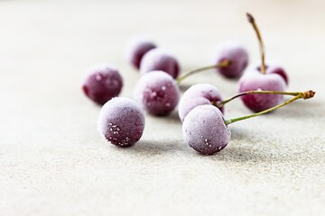 Frozen sweet black cherries covered with hoarfrost on stone background. Summer food. Useful, proper nutrition.