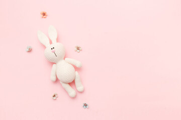 Knitted rabbit amigurumi with flowers isolated on a pink background. Baby background. Copy space, top view