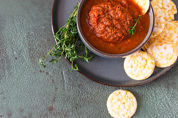 Ceramic bowl with spicy tomato sauce, tortilla chips and thyme on green stone background. Mexican food concept. Copy space. Top view.