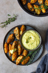 Baked crispy potato wedges with cheese sauce and thyme on black ceramic plate. Homemade snack food. Top view.