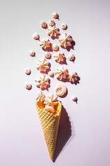 Top view of crispy ice cream waffle cone and marshmallows on pink background.