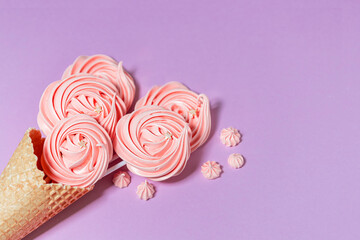 Top view of crispy ice cream waffle cone and marshmallows on pink background.