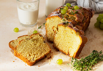 Delicious homemade grape loaf cake with thyme and sugar powder on parchment paper. Light stone background.