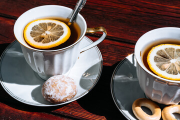 Drink tea with bagels and sweet cakes. On the mahogany table are two white cups of tea with lemon. Tea and a good time.