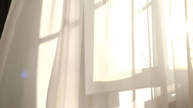 wind blows through the open window in the room. Waving white tulle near the window. sun's rays shine through the transparent tulle