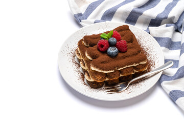 portion of Classic tiramisu dessert with raspberries and blueberries on ceramic plate isolated on white background with clipping path