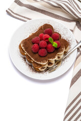 portion of Classic tiramisu dessert with raspberries on ceramic plate isolated on white background with clipping path
